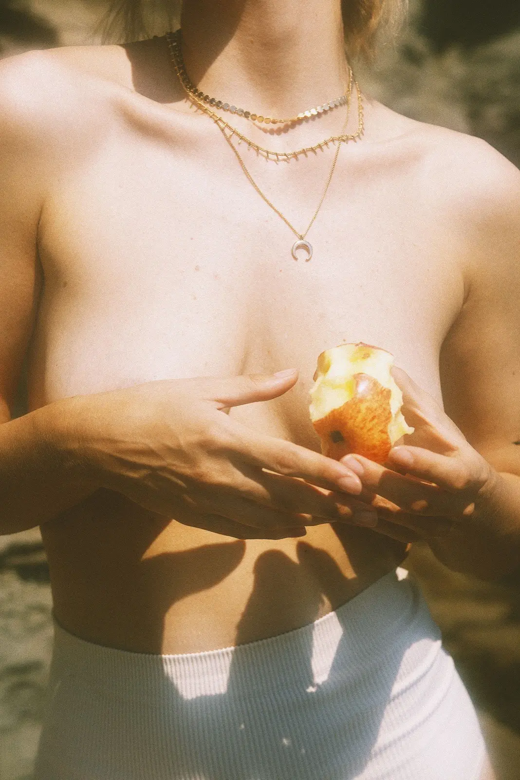 A woman holding a bitten apple in front of her chest