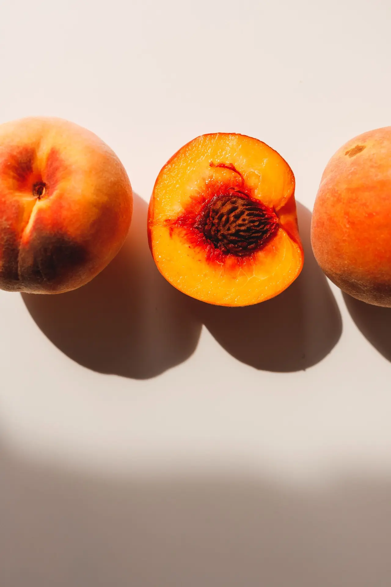 Three peaches on a pale background, the middle one cut open to show the pit